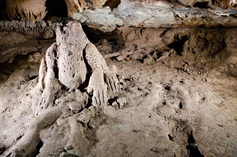 Three-dimensional sculpture depicting a 105-centimeter-tall jaguar, covered in carved spots, sitting atop a human-shaped relief. Note the small clay figures in the background, on the wall. Credit: Leslie F. Zubieta Calvert / INAH