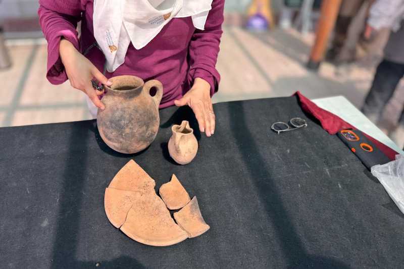 Arqueólogo apresentando o conjunto de jantar com 3.500 anos, composto por um jarro, um jarro com boca em forma de trevo e um prato, em 4 de setembro de 2025. (Foto AA)