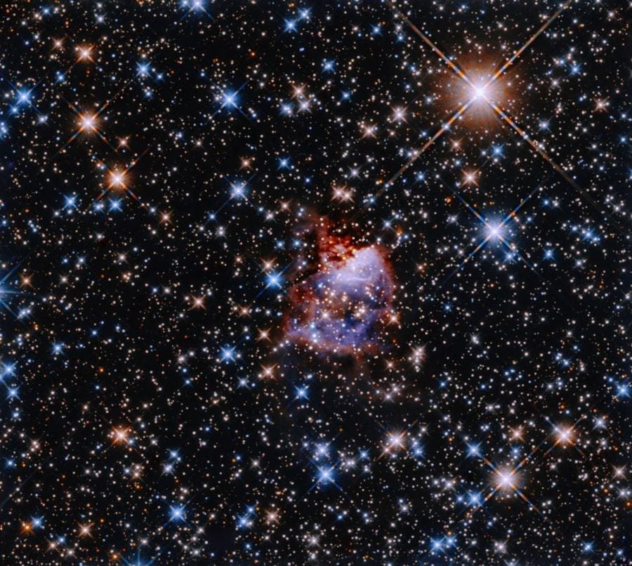 This Hubble image shows the star formation region G033.91+0.11. A central nebula lies in the center of a glittering backdrop of multicoloured stars. The nebula is reflecting light from a bright and massive young protostar. Scientists use the initial mass function to estimate the mass ratios of stars created in such starbirth regions. Image Credit: NASA, ESA, and R. Fedriani (Instituto de Astrofisica de Andalucia); Processing: Gladys Kober (NASA/Catholic University of America)