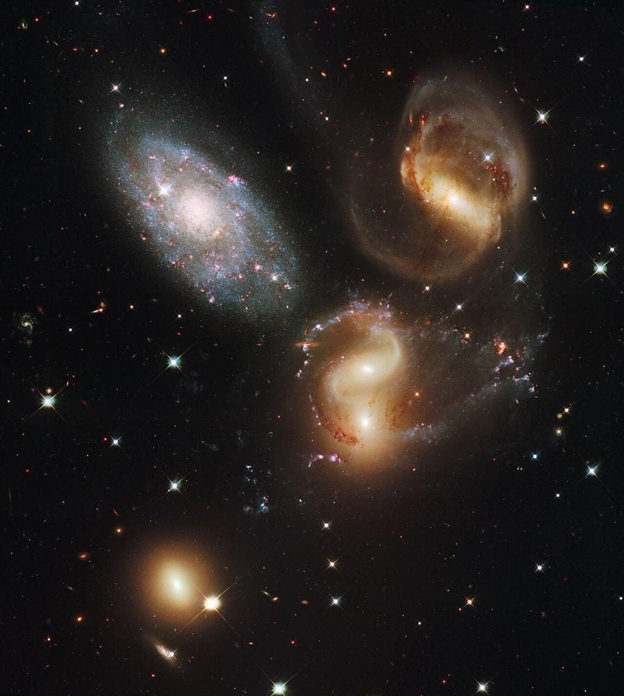 The galaxy in the upper left (NGC 7320) is not one of the members of the compact group in Stephan's Quintet. This Hubble image from 2009 shows how three of the members of the compact group are distorted, with stretched and misshapen spiral arms, and long tidal tails of gas, all lit up by countless star clusters. Image Credit: NASA, ESA, and the Hubble SM4 ERO Team. Public Domain.